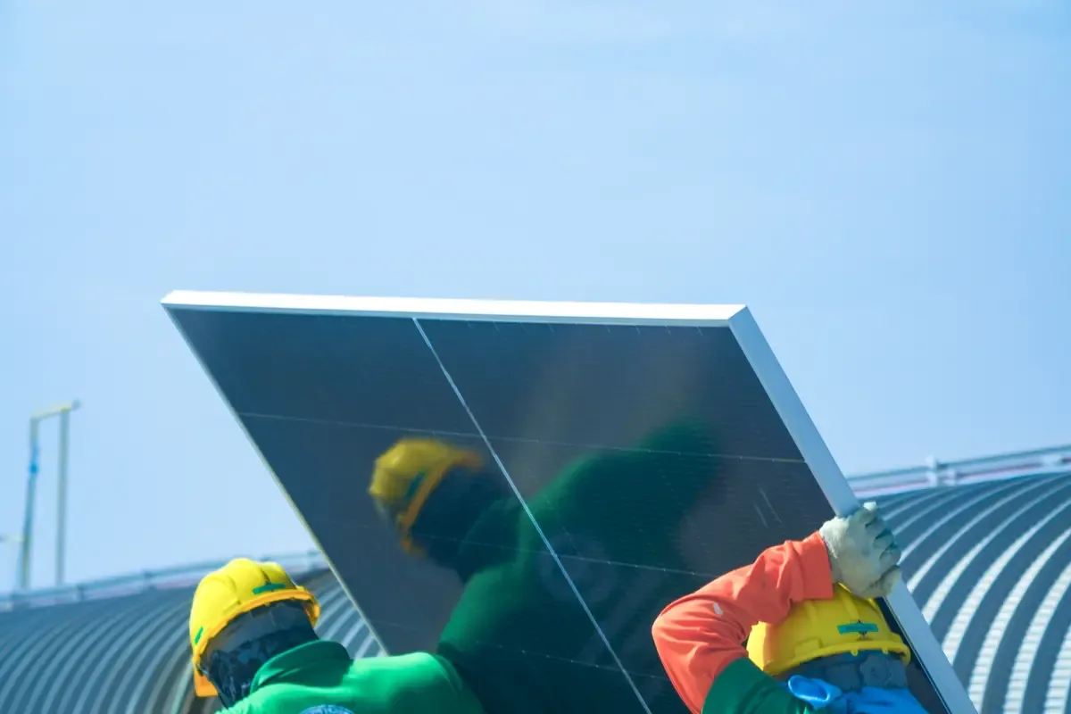 Operarios colocando un panel solar sobre una cubierta industrial curva, como las de las naves de Sabadell